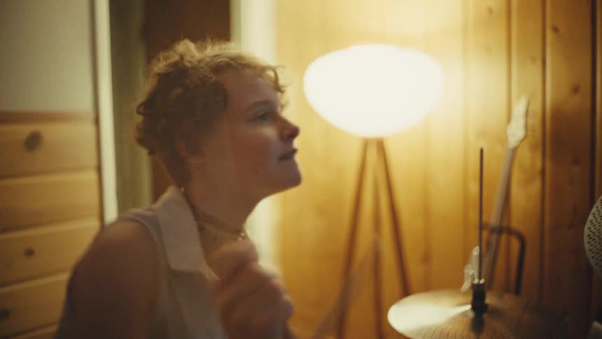 Female drummer energetically plays a drum kit in a cozy, vintage-style home music studio