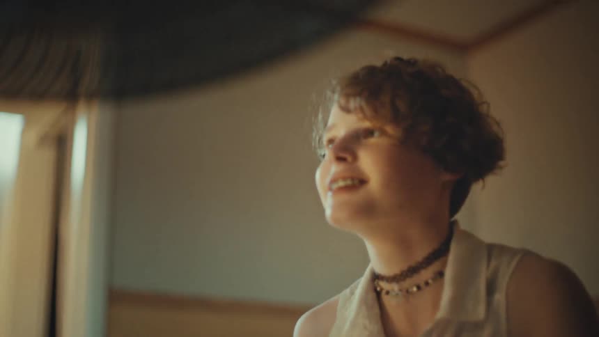 A happy young drummer with short curly hair and braces passionately plays the drums in a warmly lit room, shown in a low-angle shot