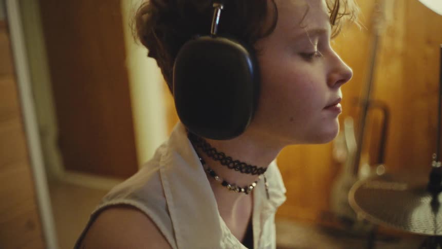 A focused young musician with an alternative style listens to music with their eyes closed in a home studio