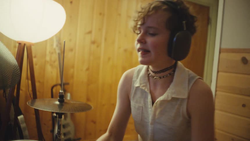 A young musician with headphones energetically plays a drum kit in a cozy, wood-paneled room
