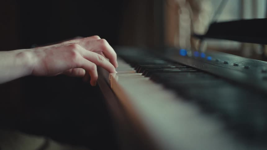 An intimate, artistic close-up shot of a person's hands gracefully playing a melody on an electric piano