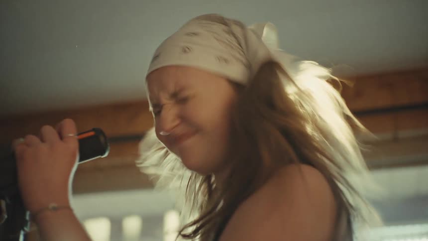 A passionate female vocalist in a bandana sings into a microphone during a band practice in slow motion