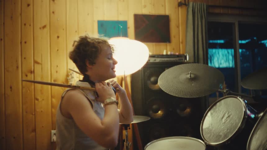 Slow motion shot of a happy young drummer taking off headphones and relaxing after a music session
