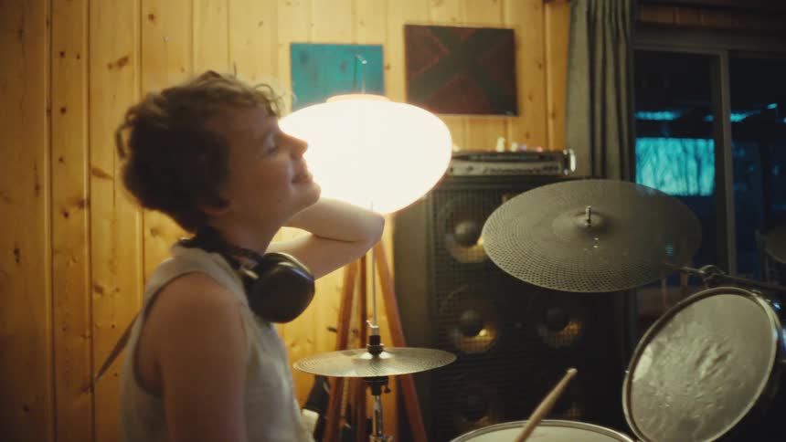 Slow motion shot of a happy young drummer taking off headphones and relaxing after a music session