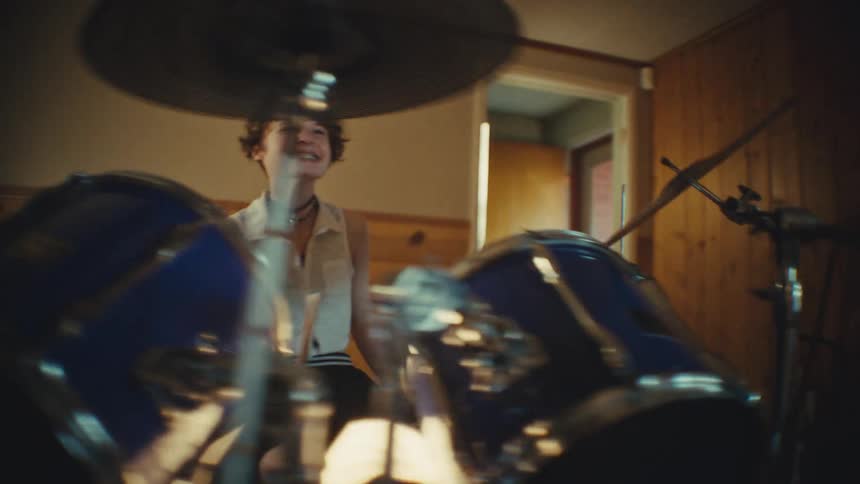 A passionate young drummer smiles and rocks out on the drum kit during an energetic band rehearsal in a home studio
