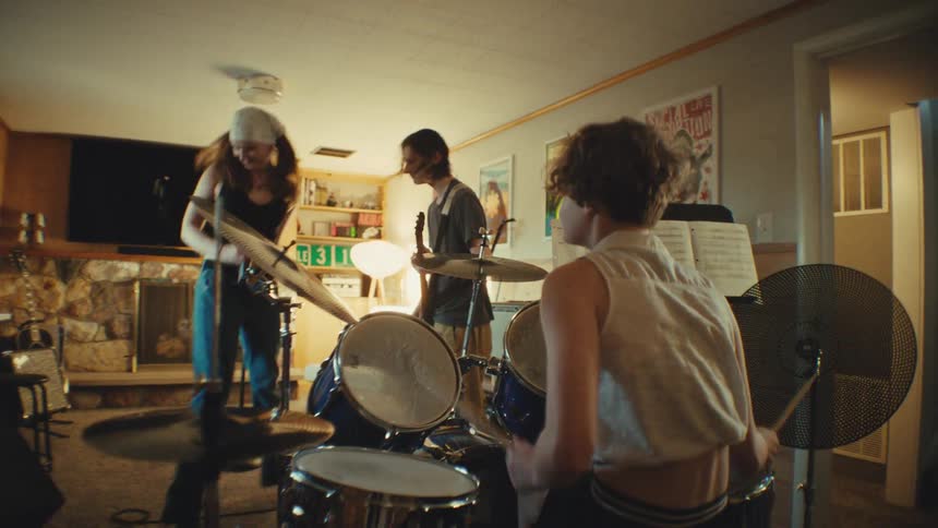 A youthful rock band energetically jams together during a rehearsal in their home basement studio