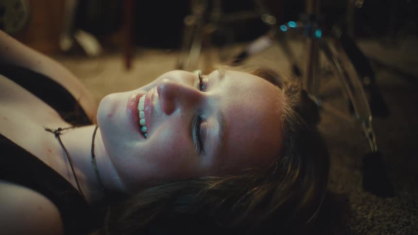 A young woman lies on the floor of a music studio, a blissful smile appearing on her face as she listens