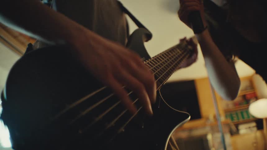 Energetic low-angle slow-motion shot of a bassist playing a five-string guitar while the lead singer passionately performs in a home studio