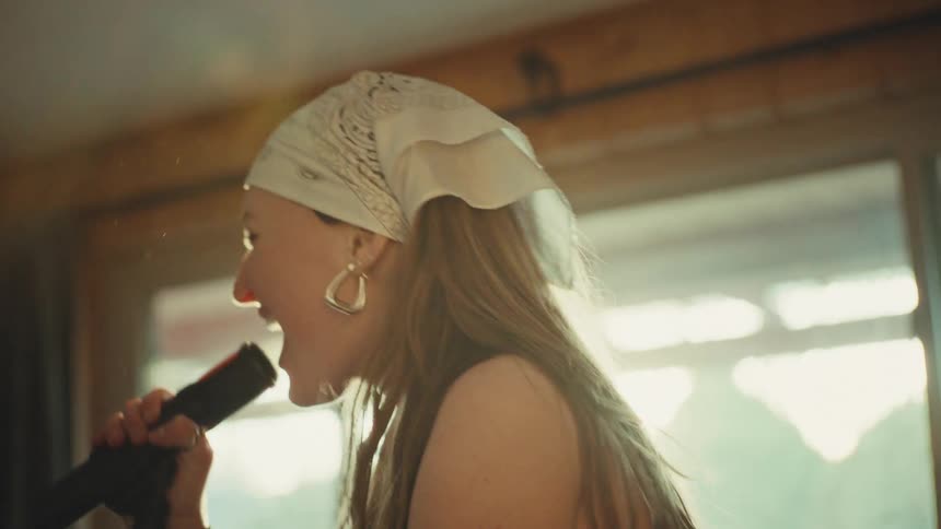 A backlit female vocalist with a bandana passionately screams into a microphone during a band practice in slow motion