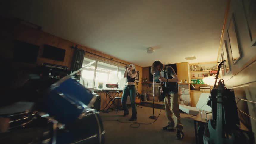 A dynamic wide-angle shot pans from the drummer to reveal a youthful band passionately rehearsing in their home studio