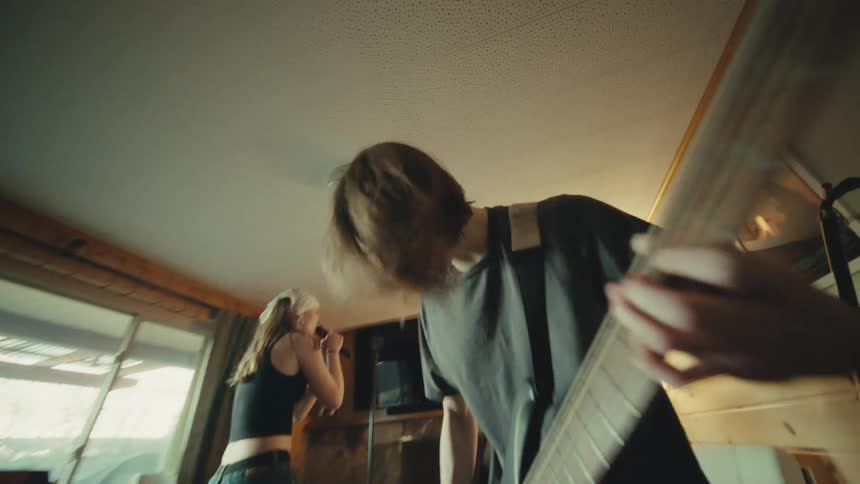 A dynamic wide-angle shot pans from the drummer to reveal a youthful band passionately rehearsing in their home studio