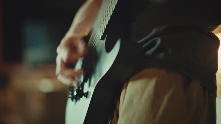 Close-up of a guitarist's hand strumming an electric guitar with energy in a dimly lit, atmospheric room