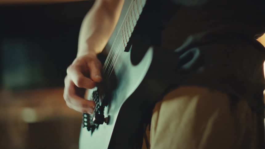 Close-up of a guitarist's hand strumming an electric guitar with energy in a dimly lit, atmospheric room