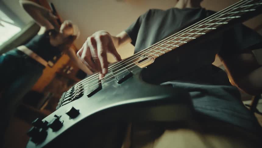 Energetic low-angle slow motion shot of a rock band rehearsal, focusing on the bassist playing and headbanging