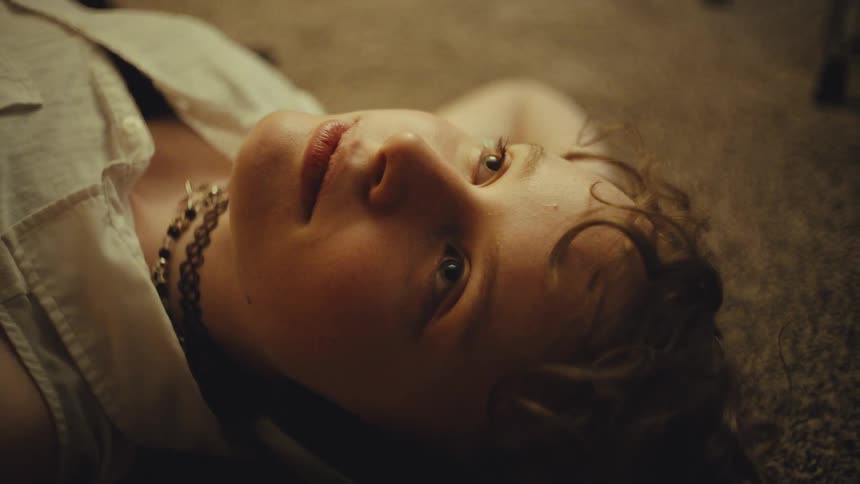 A moody cinemagraph shows a close-up of a young person's face as they lie on the floor staring into space