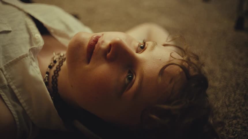 A moody cinemagraph shows a close-up of a young person's face as they lie on the floor staring into space