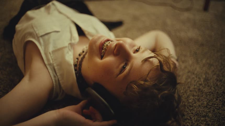 Upward-looking shot of a young person with braces relaxing on the floor and smiling while listening to headphones