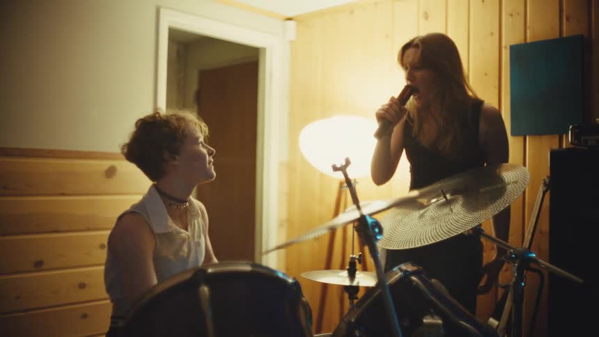 A female drummer and singer passionately rock out together during a band practice session in a home studio