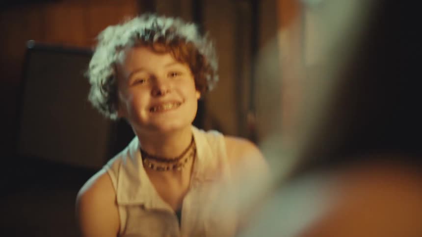 A happy teenager with curly hair and braces laughs wholeheartedly while having a fun conversation with a friend in slow motion