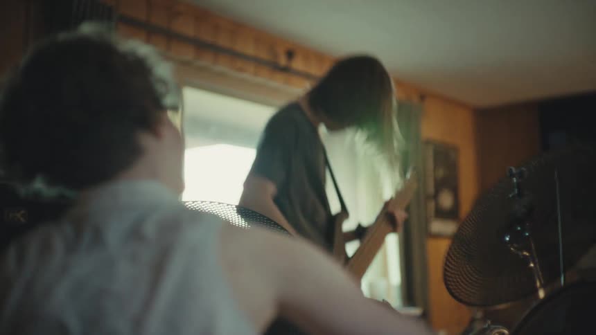A long-haired bass player headbangs with passion during a rock band practice session in a dimly lit room