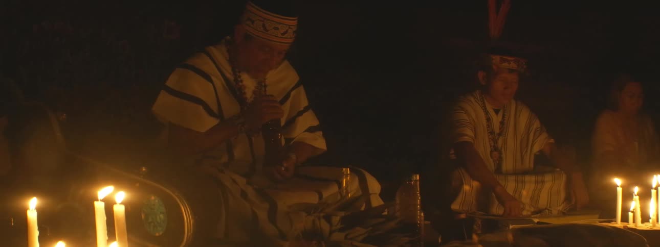 Indigenous shamans wearing traditional clothing conduct a sacred spiritual ceremony by candlelight