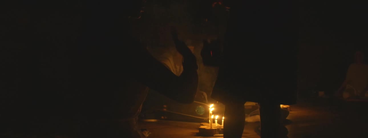 A group of people participates in a mystical candlelit spiritual ceremony in a dark room