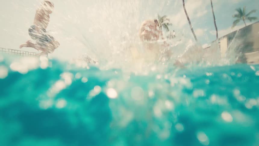 A happy group of kids leap joyfully into a swimming pool one after another in slow motion on a sunny day