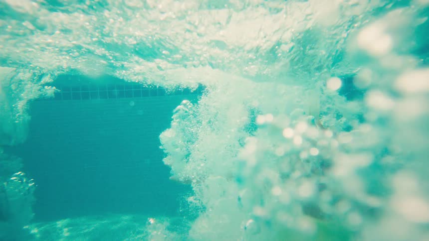A happy group of kids leap joyfully into a swimming pool one after another in slow motion on a sunny day