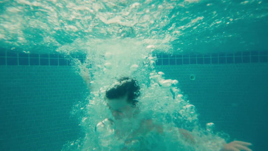 A young boy cannonballs into a swimming pool at a resort, captured in slow motion above and below the water
