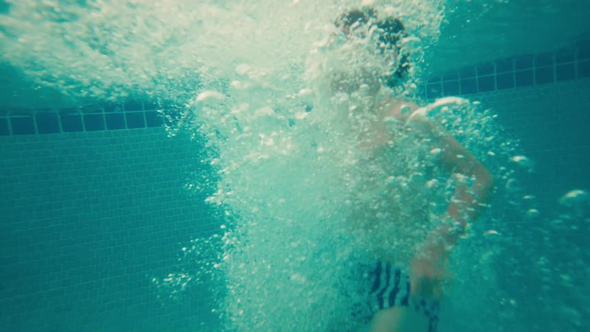 A young boy cannonballs into a swimming pool at a resort, captured in slow motion above and below the water