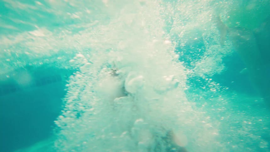A young boy jumps into a swimming pool in a cannonball, captured in slow motion from an underwater perspective