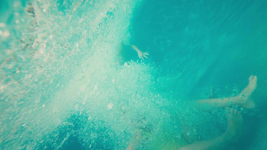 A young girl wearing goggles joyfully jumps into a pool in slow motion, with an exciting underwater view of her splash