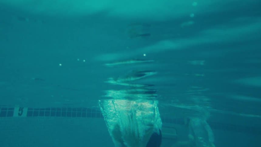 Slow motion underwater view of a young boy with goggles jumping into a swimming pool at a tropical resort