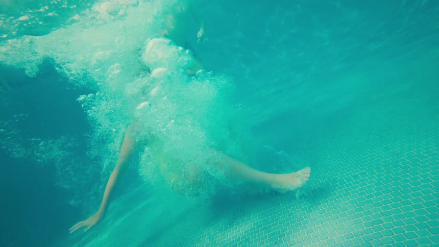 Split-level over-under shot of a person jumping into a swimming pool in super slow motion, with palm trees and a resort in the background