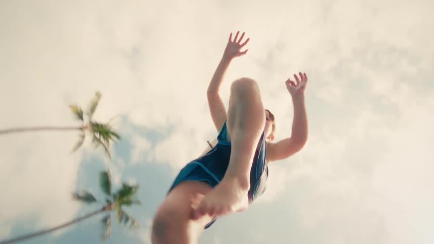 A joyful young boy in blue swim trunks jumps into a tropical swimming pool in a dynamic slow-motion underwater shot