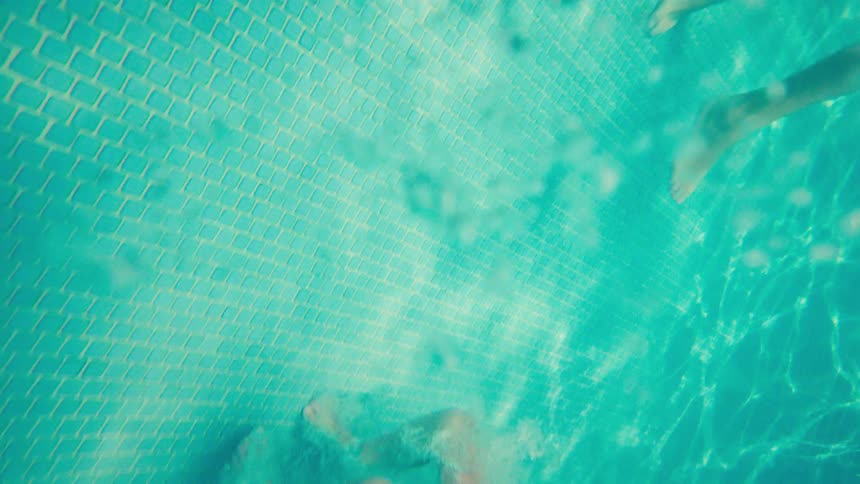 A joyful young boy in blue swim trunks jumps into a tropical swimming pool in a dynamic slow-motion underwater shot