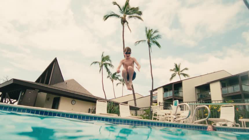 Slow motion shot of a young boy jumping into a tropical resort swimming pool, captured from an underwater perspective