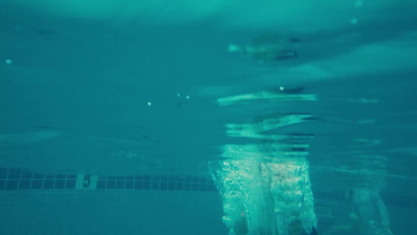 Slow motion shot of a young boy jumping into a tropical resort swimming pool, captured from an underwater perspective