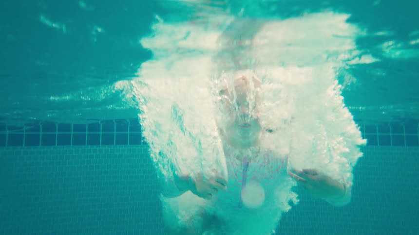 A happy young girl jumps into a tropical swimming pool in slow motion, captured with an exciting underwater splash