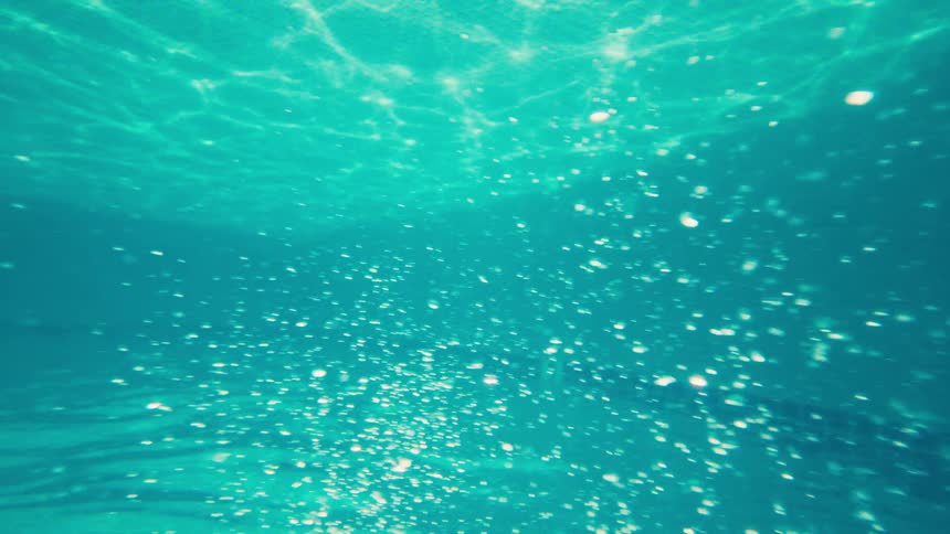 An ethereal underwater shot of sparkling bubbles rising through turquoise water illuminated by sunlight
