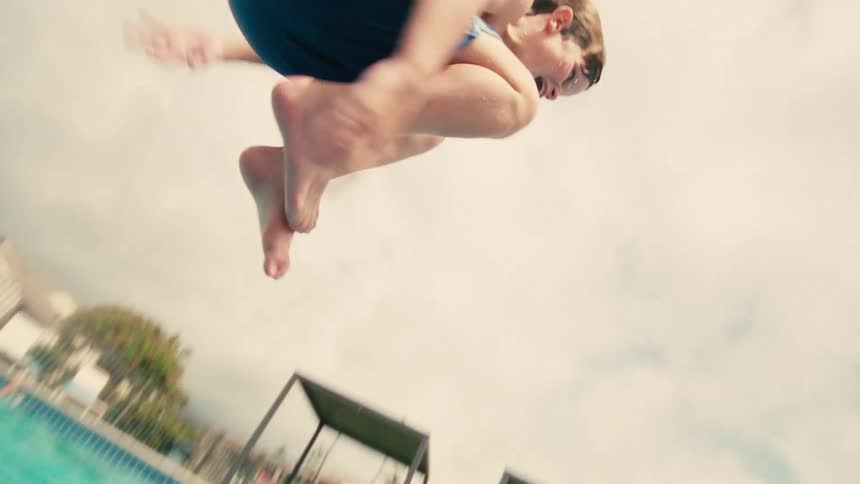 Slow motion underwater view of a happy young boy jumping with a splash into a bright blue swimming pool