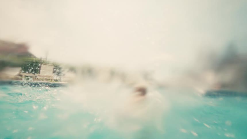 A young girl emerges from underwater with a playful splash in a sunny resort swimming pool