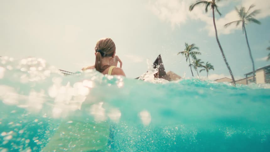 A young girl emerges from underwater with a playful splash in a sunny resort swimming pool
