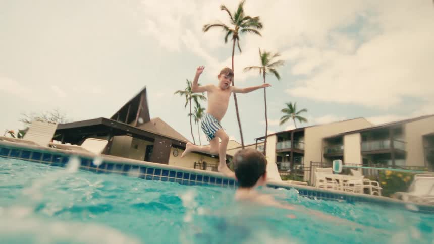 A young boy makes a big splash as he jumps into a tropical resort pool in dynamic slow motion