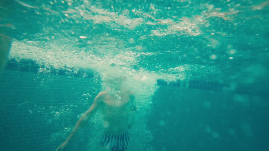A young boy makes a big splash as he jumps into a tropical resort pool in dynamic slow motion