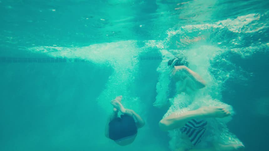 A young boy jumps into a tropical resort swimming pool in an exciting slow-motion shot that follows him underwater