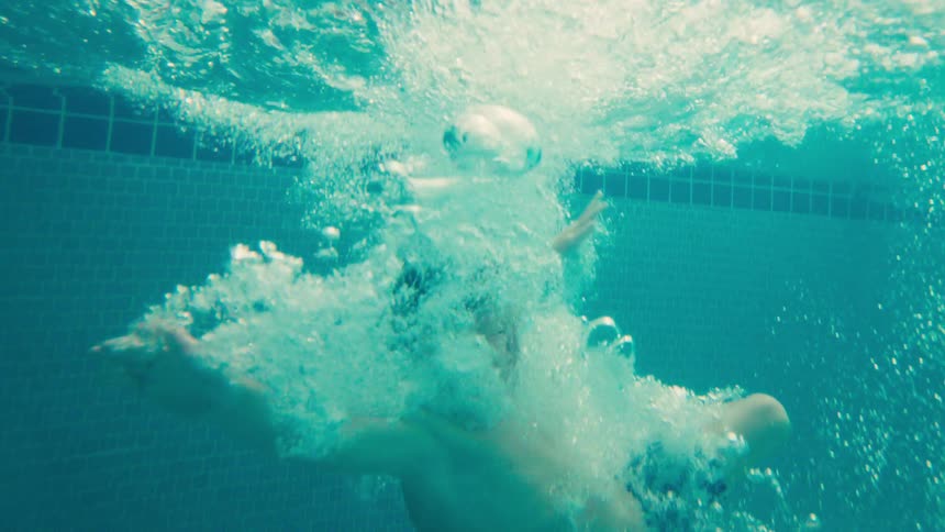 A young boy jumps into a swimming pool, captured in a stunning slow-motion underwater shot with bubbles