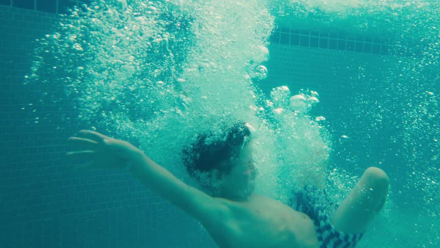 A young boy jumps into a swimming pool, captured in a stunning slow-motion underwater shot with bubbles