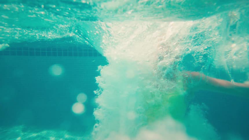 Kids joyfully jump into a swimming pool in slow motion, with the camera capturing the energetic splash from an underwater perspective
