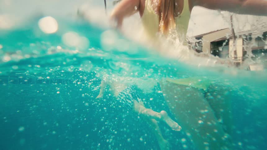 Slow motion split-level shot of two children joyfully splashing and swimming in a tropical resort pool